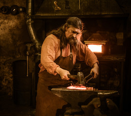 Senior blacksmith forging the molten metal on the anvil in smithy