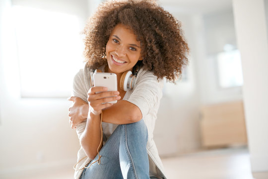 Smiling mixed-race girl sitting on floor at home and using phone