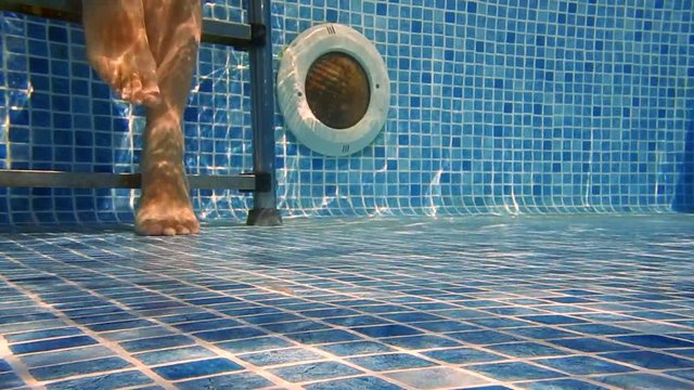 Female feet walking in a swimming pool with a step ladder in background. Underwater. Slow motion.