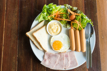 Fototapeta na wymiar American breakfast with bread, fried eggs, sausage, bacon and salad on wood background