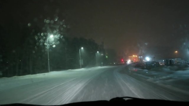 Timelapse of driving a car during snowstorm at night through city.