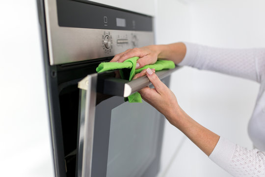 Junge Frau putzt in der K&uuml;che den Backofen