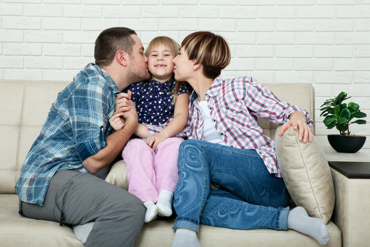 Family relaxing on sofa at home. The family father, mother and happy daughter sitting on sofa hugging and looking at camera.