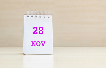 Closeup surface note book with purple 28 nov word in page on blurred brown wood desk and wood wall textured background with copy space under window light