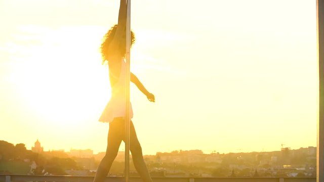 Sexy attractive girl poledancer performs advanced pole dance tricks at sunset on portable dancing stage over the skyline