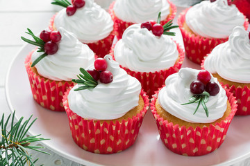 Christmas cupcakes with vanilla frosting, cranberries and rosemary on white wooden background. Selective focus