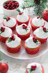 Christmas cupcakes with vanilla frosting, cranberries and rosemary on white wooden background. Selective focus