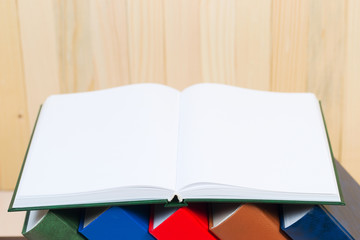 Open book, stack of hardback books on wooden table.