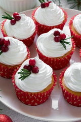 Christmas cupcakes with vanilla frosting, cranberries and rosemary on white wooden background. Selective focus