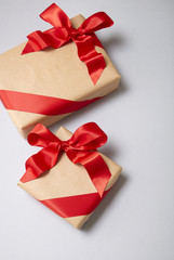Christmas presents wrapped in brown paper with red silk bows on a soft grey background with blank space at side