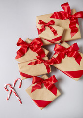 Christmas presents wrapped in brown paper with red silk bows and candy canes on a light grey...