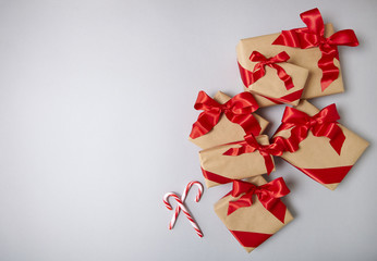 Christmas presents wrapped in brown paper with red silk bows on a pale grey background, with candy canes and blank space at side