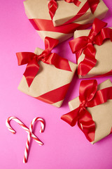 Christmas gifts wrapped in brown paper with red silk bows and candy canes on a bright pink background