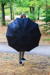 Young caucasian girl enjoying a rainy day in the countryside.. She goes with an umbrella against the rain. The forest is very colorful. 