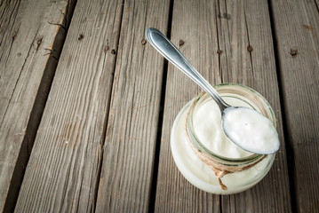 Homemade organic yogurt in a jar with a spoon on a rustic wooden table, copy space
