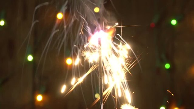 burning sparkler on a background of flashing garland
