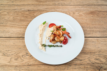 Snack to beer. Shrimp with herbs, tomatoes and cheese sauce. Served on a white plate on old wooden table