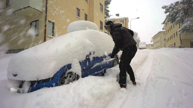 A man digging out his car on a street in full snow chaos.