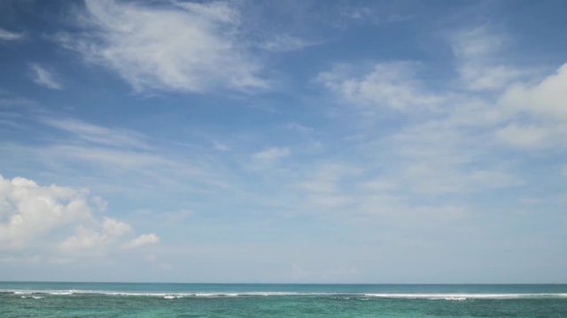 Airplane landing on island Bali airport under blue sea with waves. Cinematic shot of overhead flying aircraft with beautiful ocean on cloudy sky background. Focal length 50 mm. Slow motion