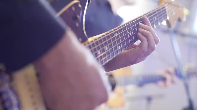 Playing guitar close-up slow motion macro. Guitarist hands pressing chords with fingers on electric guitar. Musician performs solo during concert in night club. Inspiration rehearsal boys band concept