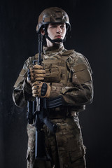Man in military uniform with assault rifle on background of dark wall. Defender of his homeland.
