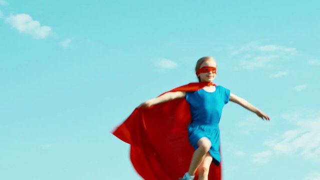 Happy super hero girl child 7-8 years old running and spinning against the blue sky. Zooming