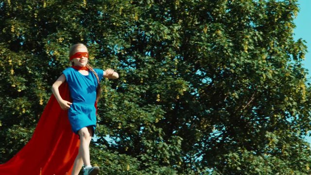 Happy superhero girl child 7-8 years old running against the blue sky. Zooming