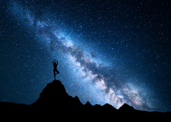 Milky Way with silhouette of a standing woman practicing yoga on the top of mountain. Landscape...