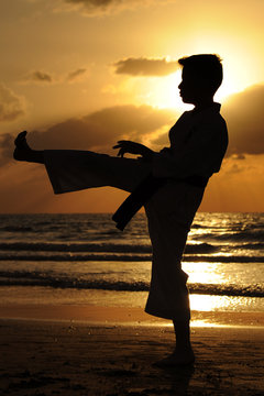 Sunset silhouette of a boy practicing karate on the beach