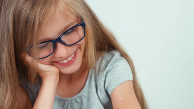 Portrait cute student girl with long blond hair 7-8 years in glasses reading book and laughing at camera. Zooming
