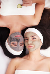 Home spa. Two women holding pieces of cucumber on their faces lying the bed.