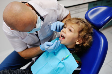 children's dentist examines the mouth baby boy with curly hair