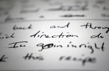 Lyrics written on paper in black ink close up. Focus on the word 