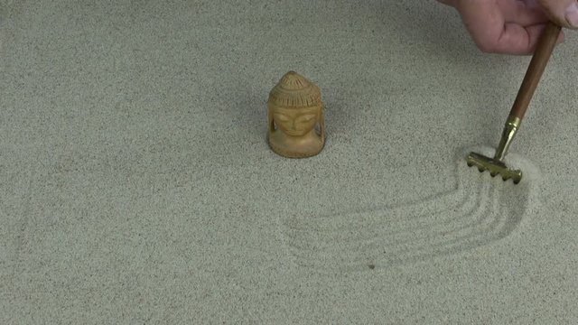 Man making zen garden with sand and Buddha head with the help of mini rake