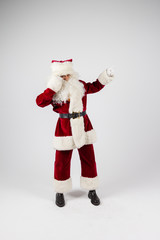 Santa Claus in eyeglasses and red costume standing on white background make a point with hands and looking into camera. Medium long shot