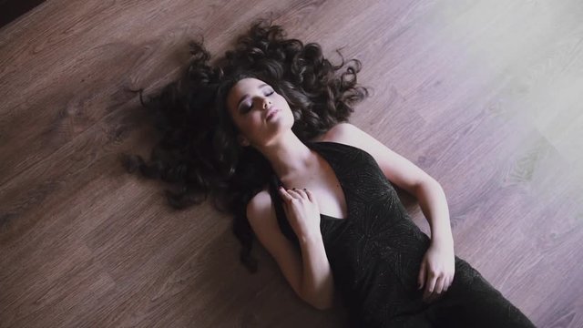 Sexy caucasian woman is lying on the floor in evening dress, beautiful girl with long hair in teasing dress, pretty woman holds her hand over the finery