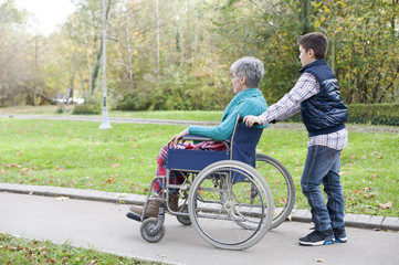 Grandson is pushing his grandmother in a wheelchair at autumn park