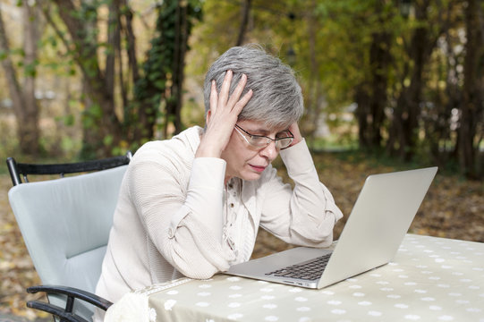 Middle Aged Worried Woman In A Park Using Laptop Computer