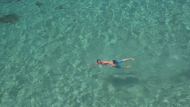 AERIAL: Active young sportsman swimming front crawl in ocean towards the shore