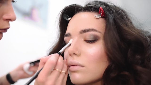 Make up stylist makes smokey eyes effect for woman at photo shoot, make up for beautiful caucasian model, girl comes to beauty fashion salon