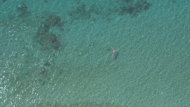 AERIAL: Cheerful guy swimming starfish float and relaxing in crystal clear ocean