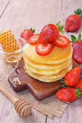Delicious pancake with fresh strawberry on top with honeycombs in glass bowl on wooden background, Stack of pancakes on the table.