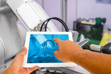 Industry 4.0 and Augmented reality for industry concept. Hand holding tablet with A/R system control application on automate robot arm in smart manufacturing background.