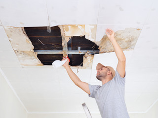 man cleaning mold on ceiling.Ceiling panels damaged huge hole in - 126490362