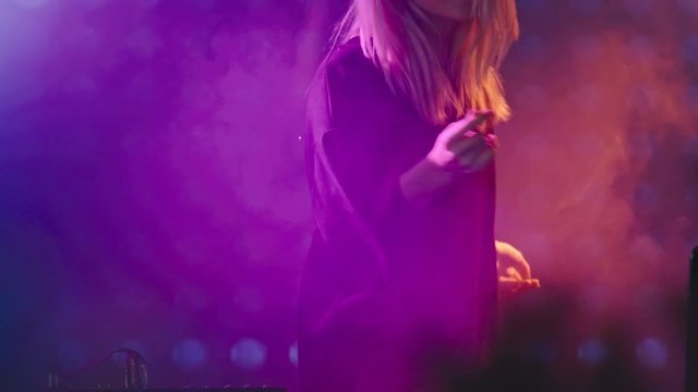 Female blond DJ dancing on stage of nightclub, then playing set on decks for audience 