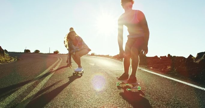 Skateboarders bombing down steep hill at sunset