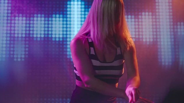 Medium shot of laughing seductive female DJ with blond hair dancing in club behind decks and mixing tracks 