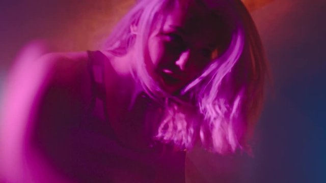Handheld shot with blur of female DJ with blond hair playing set in nightclub