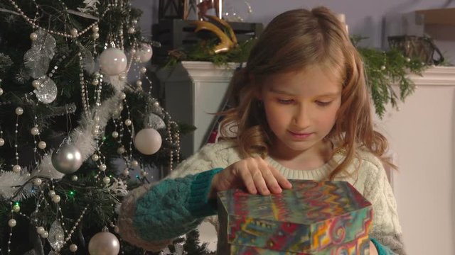 girl opening gift near Christmas tree