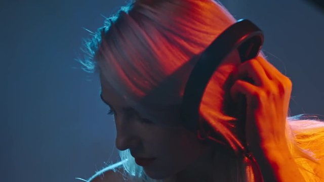 Slow motion of blond female DJ dancing and playing set with professional mixer console